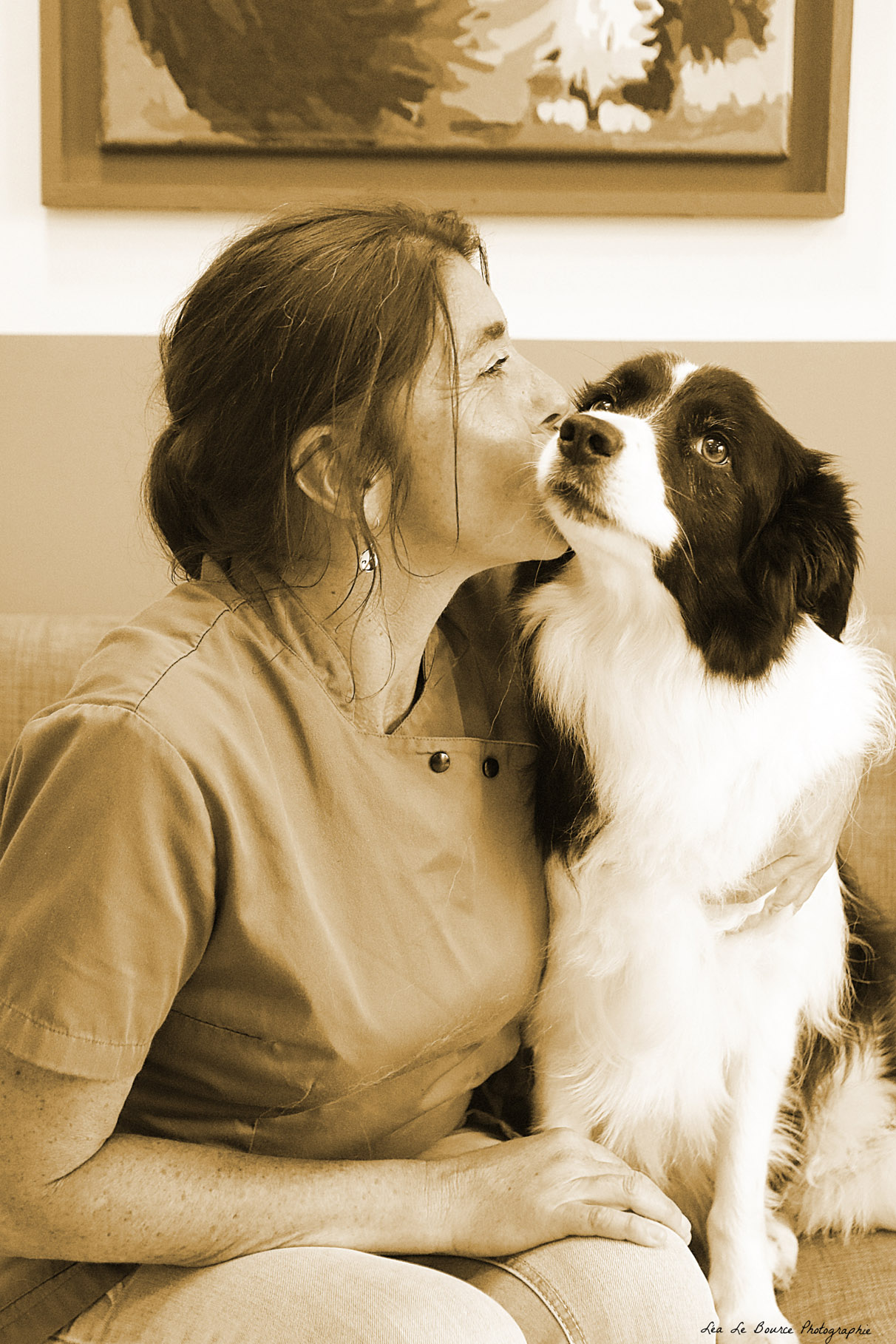 Auxilière vétérinaire qui embrasse la joue d'un border collie. La photo est en sépia.